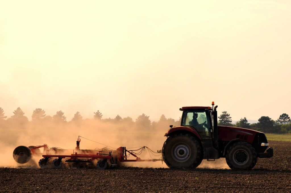 A tractor harvests the farm's yield and drags up a bunch of sand and dust